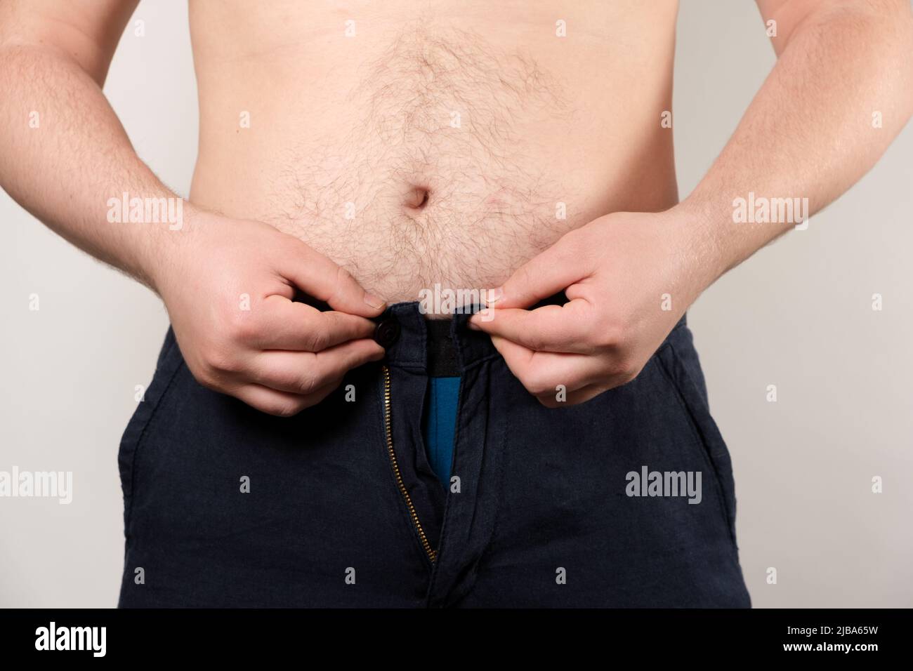 Un uomo cerca di allacciare i suoi piccoli pantaloni. Il concetto di obesità maschile, peso in eccesso Foto Stock