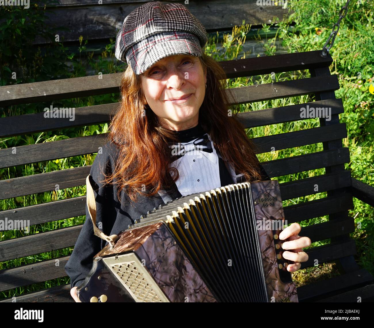 Donna anziana con capelli rossi e un cappellino si siede all'esterno e suona una fisarmonica a bottoni diatonica Foto Stock