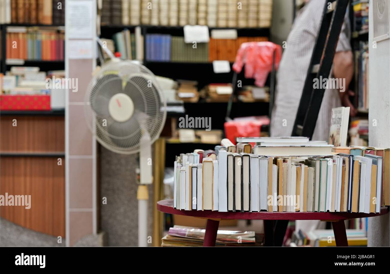 Riga di molti vecchi libri usati esposti in locale libreria antiquario, persona sfocata e più scaffali sfondo Foto Stock
