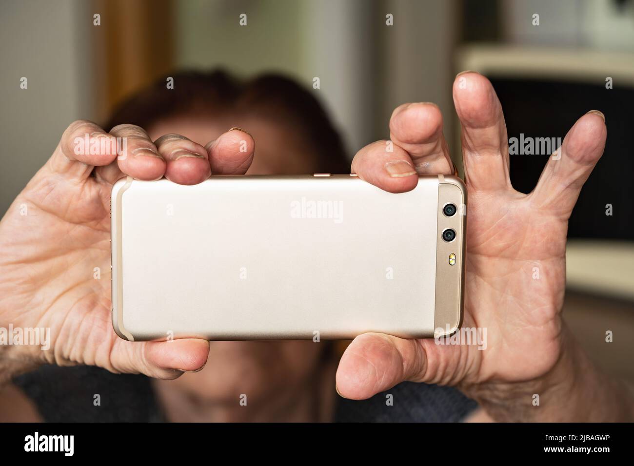 Telefono cellulare color oro rosa con due lenti tenute da mani anziane, volto sfocato in background - selfie concetto Foto Stock