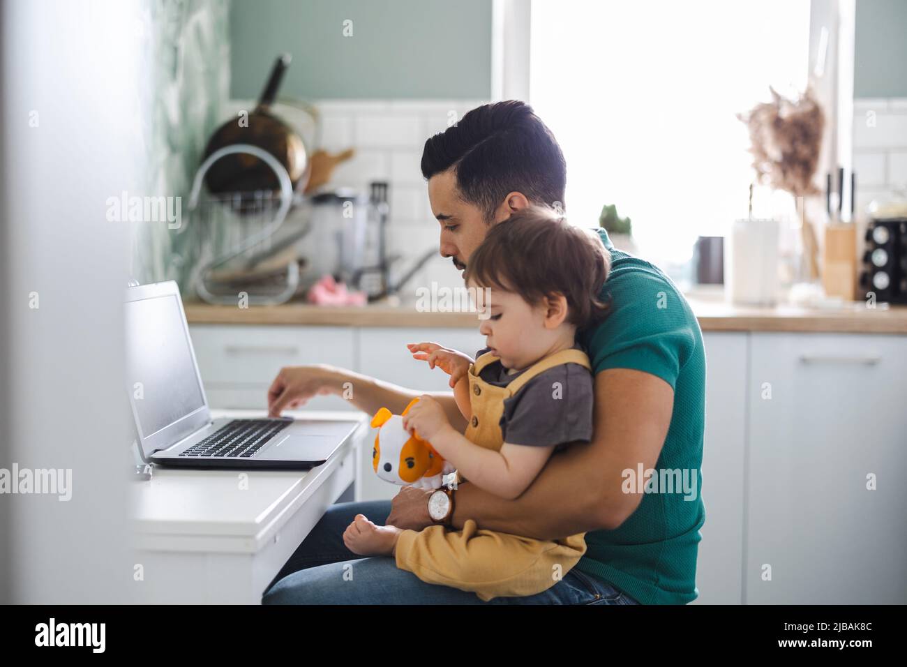 Papà che lavora su un computer portatile con un bambino seduto in grembo Foto Stock