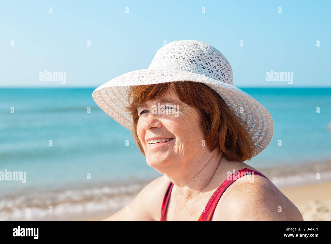 Una donna anziana in un cappello ride sulla riva del mare in una giornata di sole, close-up.Happy giorni estivi. Foto Stock
