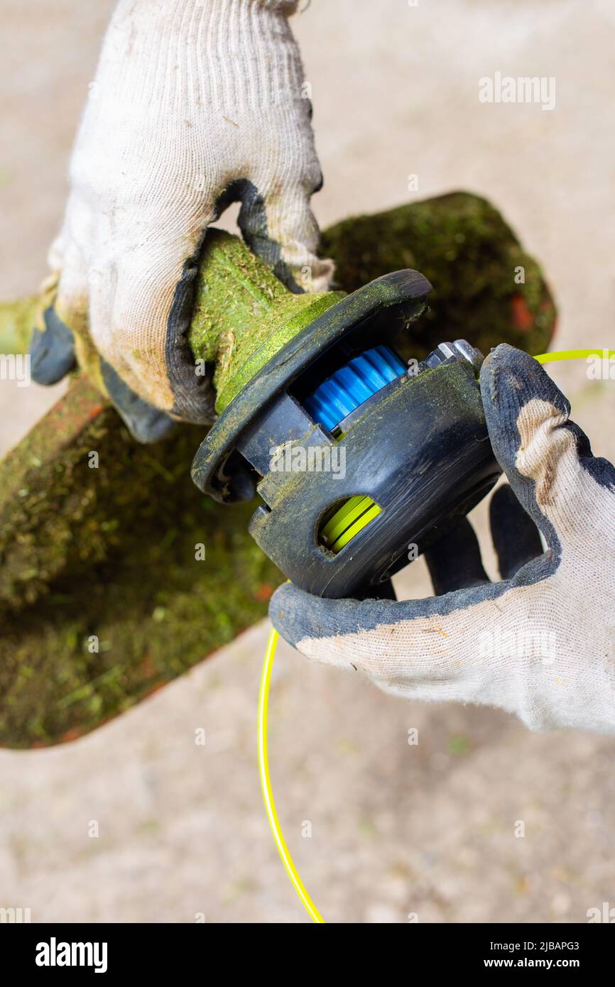 Il giardiniere mette la testina del rifinitore sul rasaerba. Sostituzione della linea su un rasaerba. Foto Stock