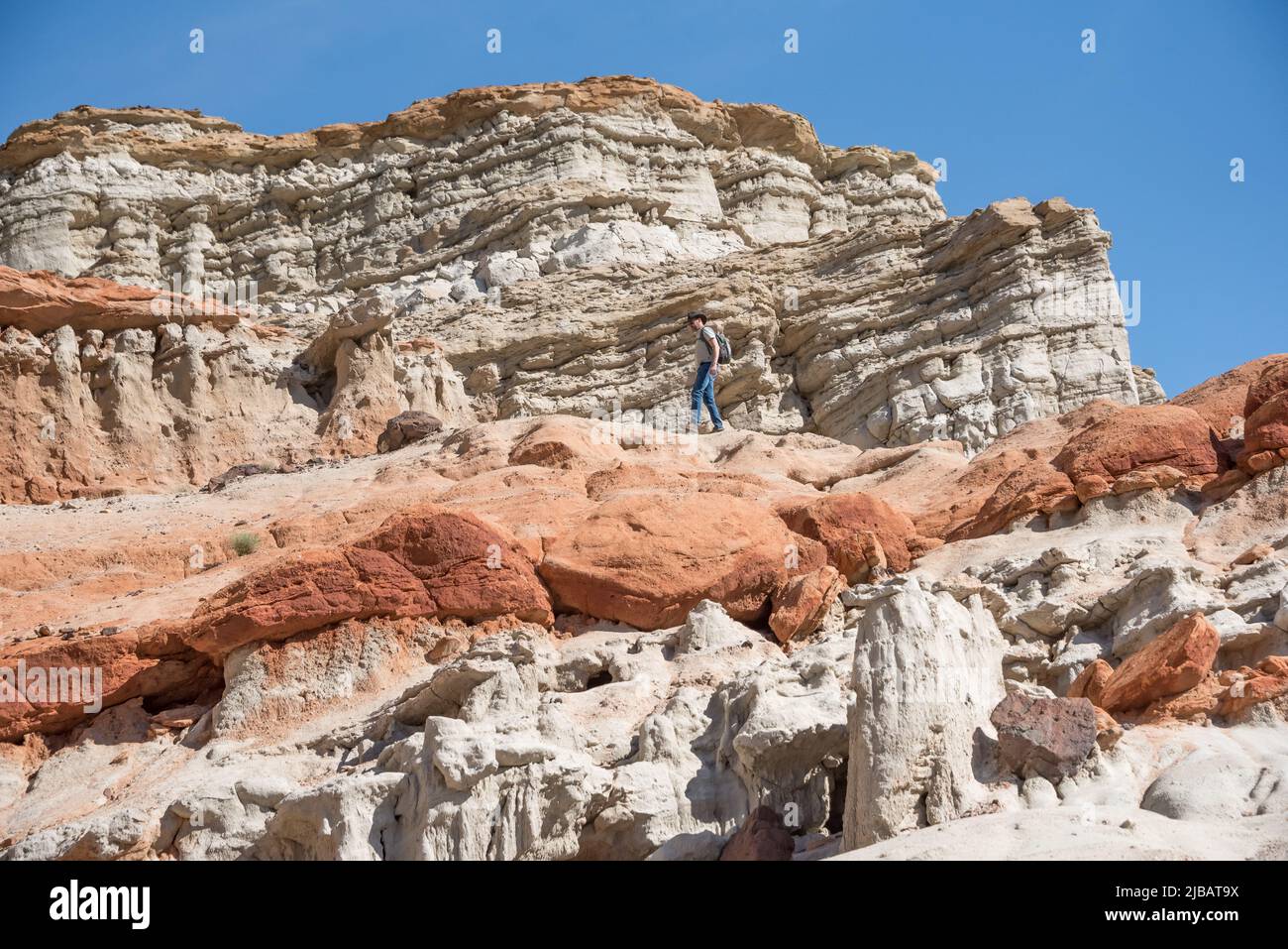 Un escursionista di mezza età in jeans esplora uno strato elevato di arenaria rossa in Hagen Canyon nel Red Rock Canyon state Park della California, a nord di Mojave. Foto Stock