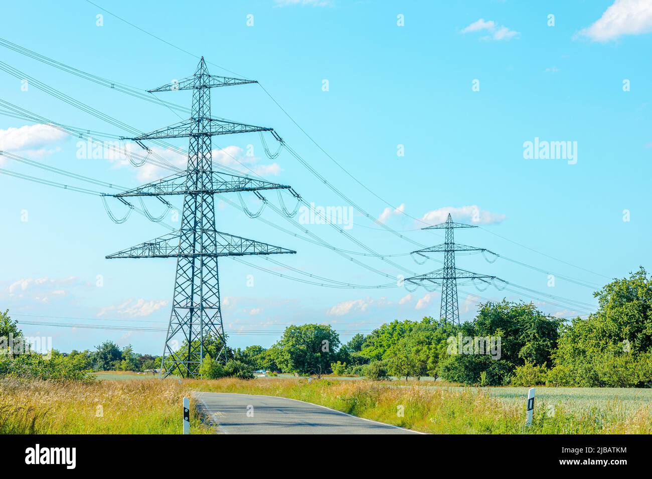 Rete elettrica di poli su un panorama di cielo blu e prato verde. Foto Stock