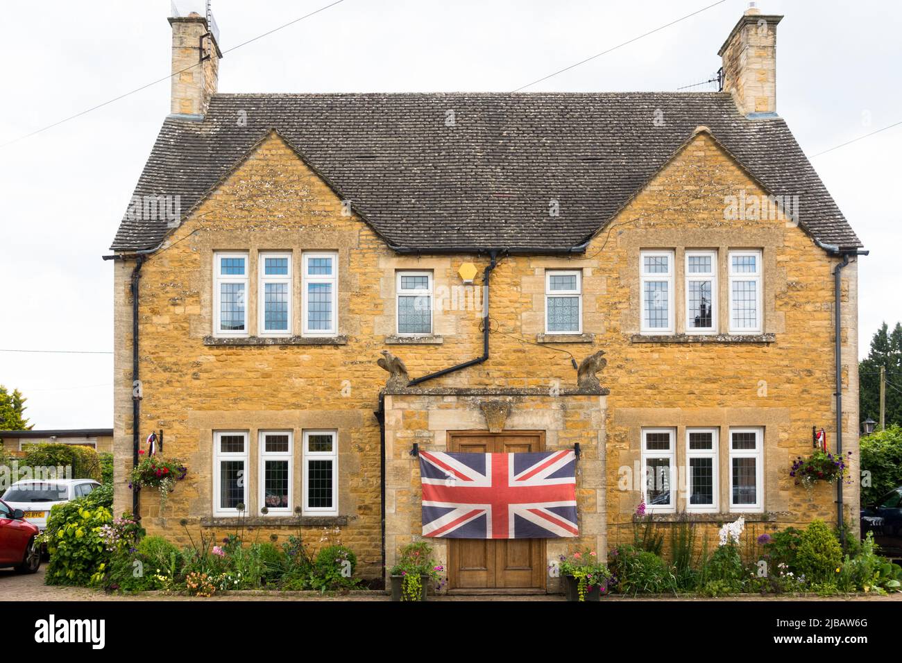 Grande Union Jack bandiera sulla porta di una casa in pietra di colore a nido d'ape tradizionale a Bourton sul villaggio d'acqua Foto Stock