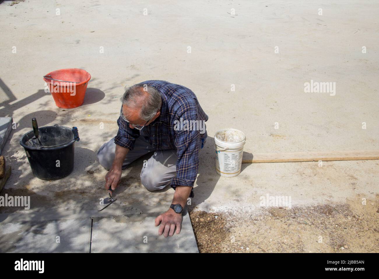 Immagine di un uomo anziano sulle ginocchia che fissa un vialetto con cemento. Riferimento al lavoro in vecchiaia Foto Stock