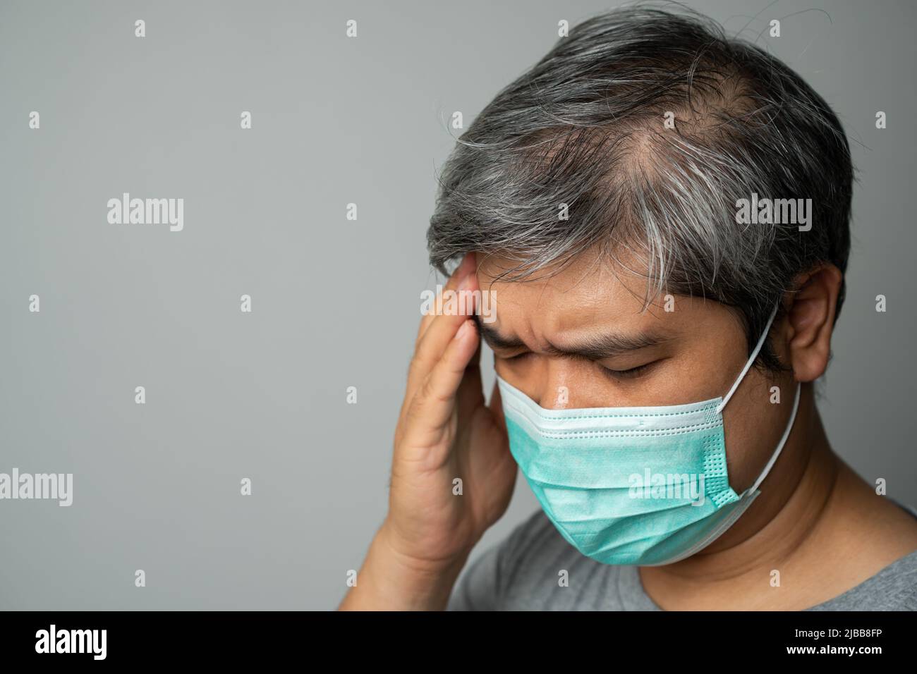 Uomo asiatico malato che indossa una maschera medica e prendere una mano per tenere il mal di testa nella testa. Concetto di protezione coronavirus pandemico e respiratore Foto Stock