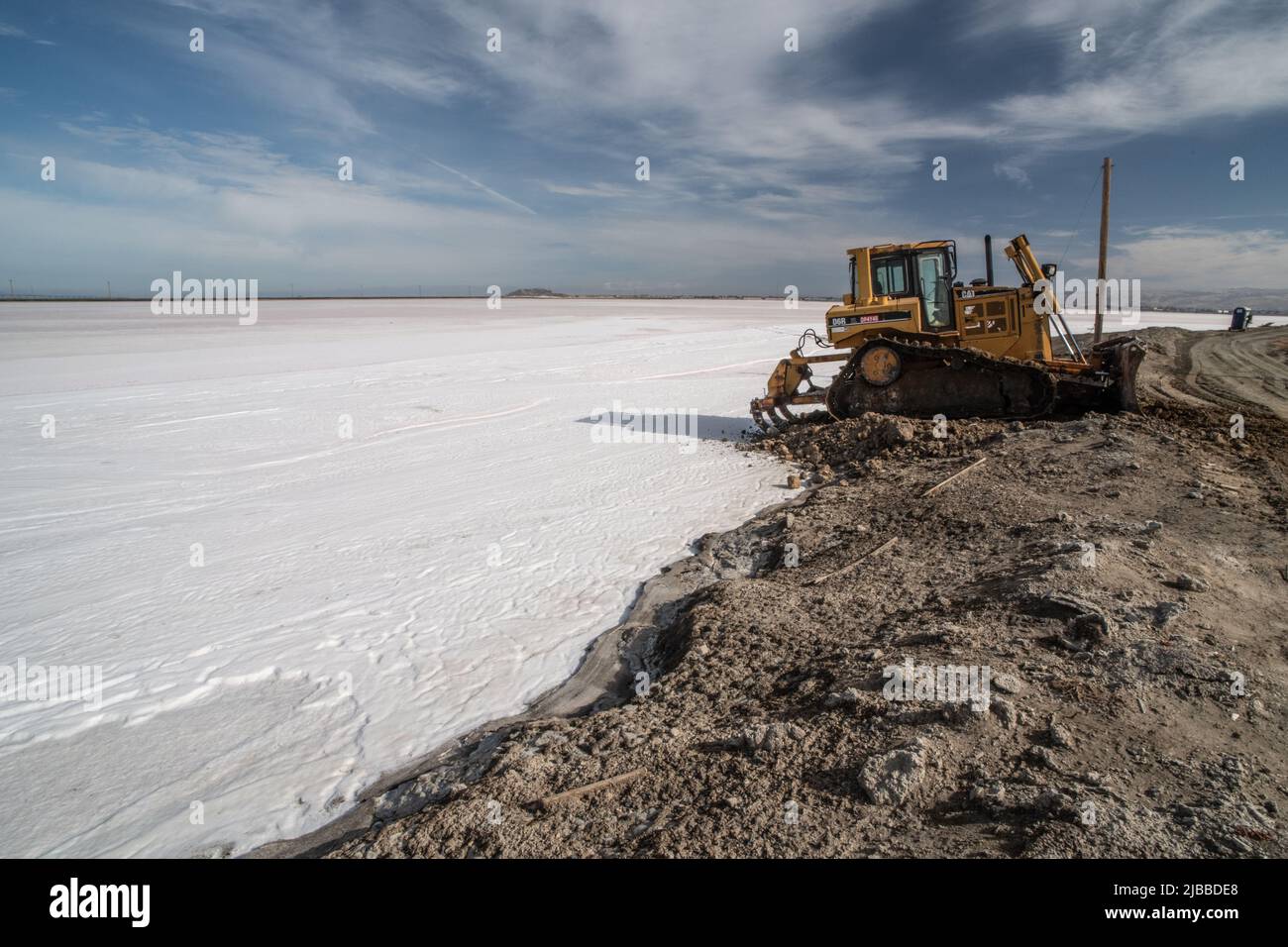 Un bulldozer al bordo di un campo di sale dove un laghetto di sale era evaporato, presto il mare sarà raccolto. Foto Stock
