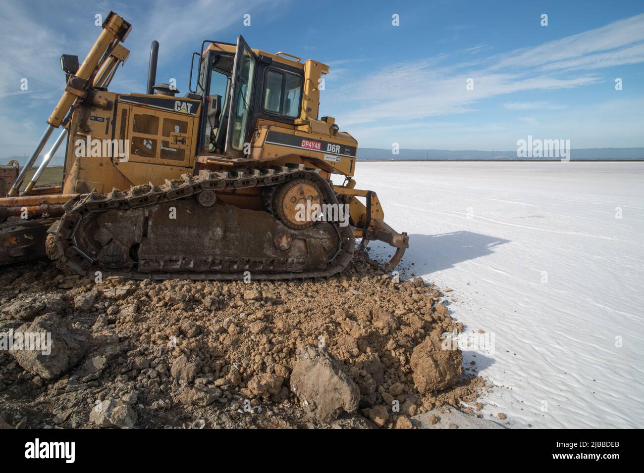 Un bulldozer al bordo di un campo di sale dove un laghetto di sale era evaporato, presto il mare sarà raccolto. Foto Stock