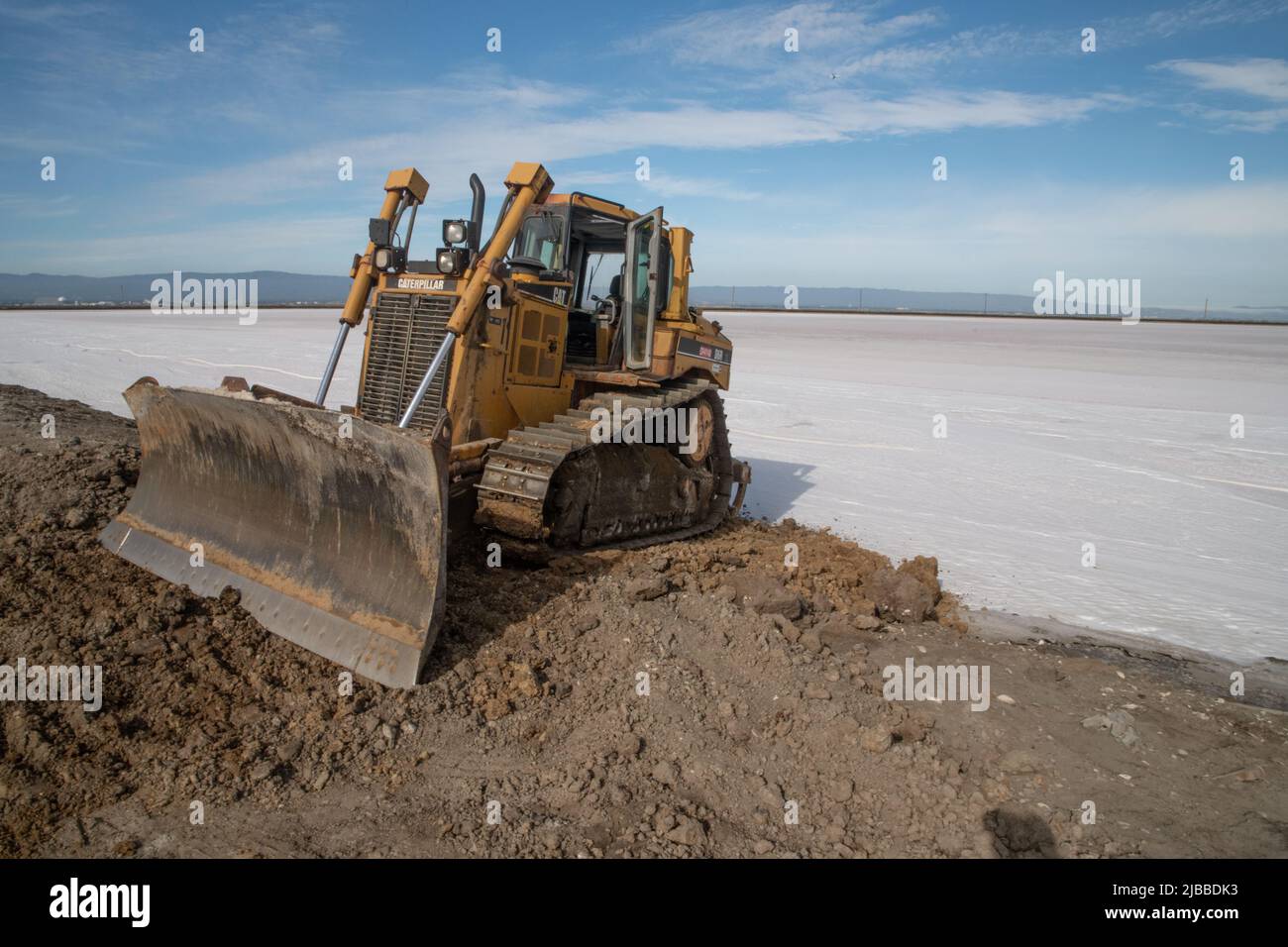 Un bulldozer al bordo di un campo di sale dove un laghetto di sale era evaporato, presto il mare sarà raccolto. Foto Stock