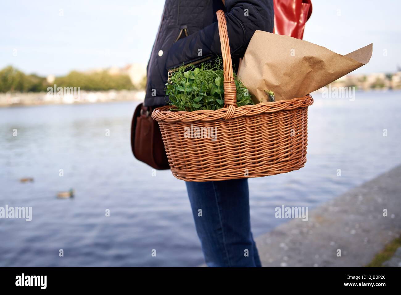 Donna in piedi alla riva del fiume Moldava a Praga con un cestino di microgrene e generi alimentari dal mercato agricolo di Naplavka Foto Stock