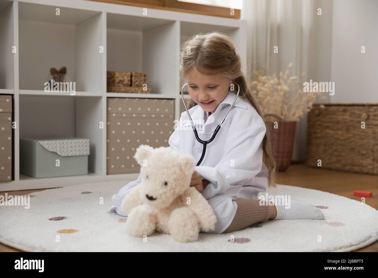 Bambino in cappotto utilizzare stetoscopio ascoltare heartbeat di orso giocattolo Foto Stock