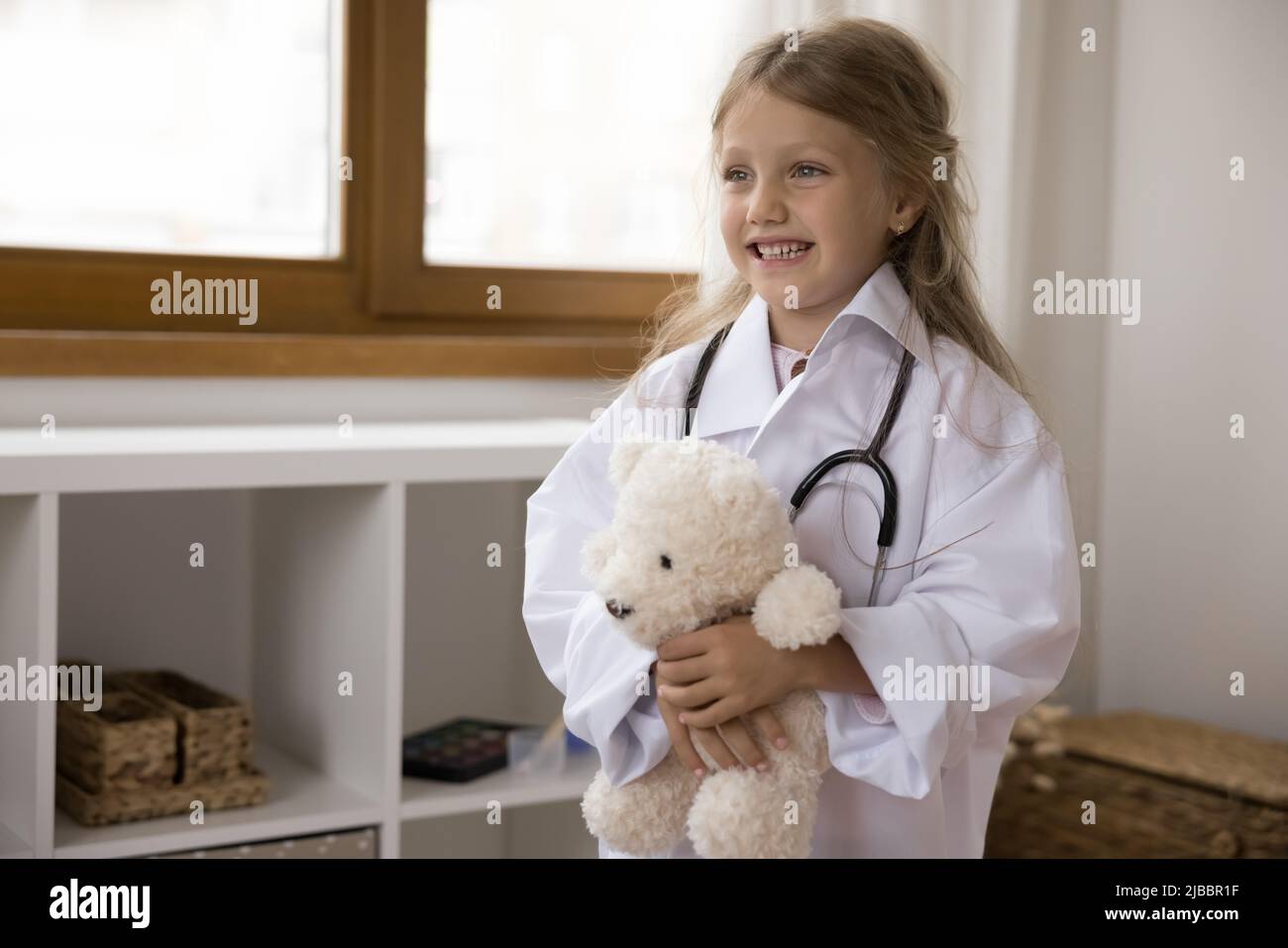 Bambina indossare cappotto bianco tiene ripieno giocattolo gioco medico Foto Stock