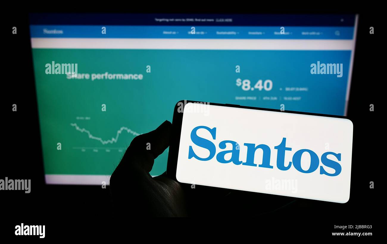 Persona che detiene il telefono cellulare con il logo della società australiana di petrolio e gas Santos Ltd. Sullo schermo di fronte alla pagina web. Mettere a fuoco sul display del telefono. Foto Stock