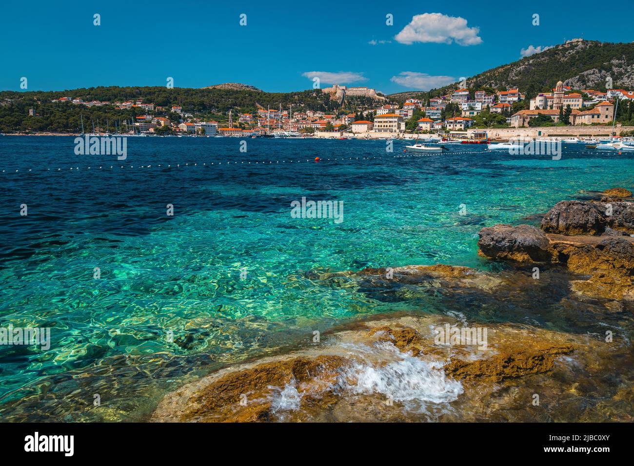 Famosa meta di viaggi e vacanze al mare. Bella spiaggia con costa rocciosa e pittoresca città di Hvar sullo sfondo, isola di Hvar, Dalmazia, Croa Foto Stock