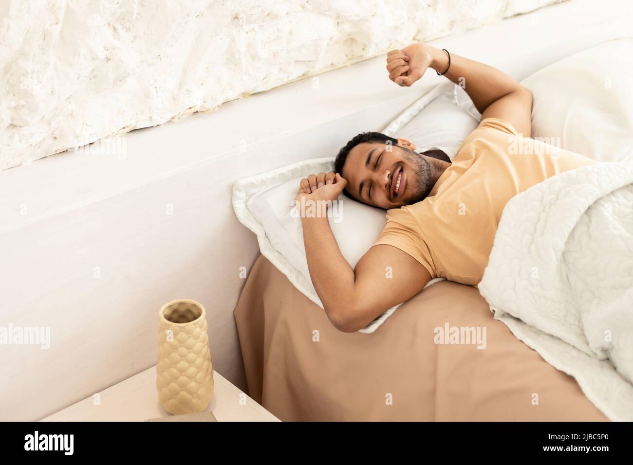 Joyful Arabic Man Awakening Stretching Arms Lying in Bedroom Indoor Foto Stock