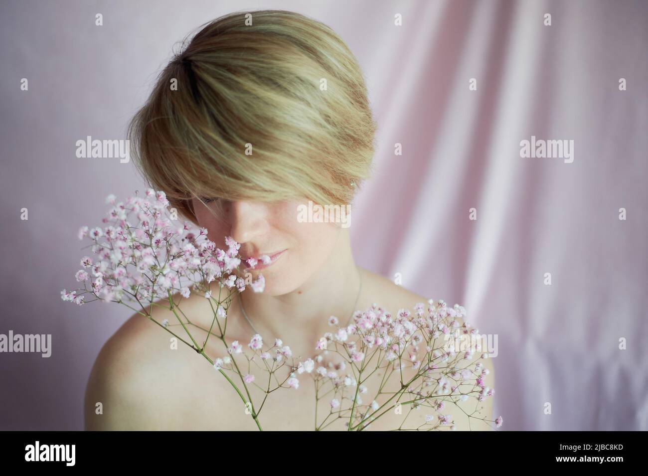 Ritratto di una ragazza su sfondo rosa con fiori. Tenerezza e femminilità. La sfera della bellezza e della salute delle donne. Taglio corto, capelli biondi Foto Stock