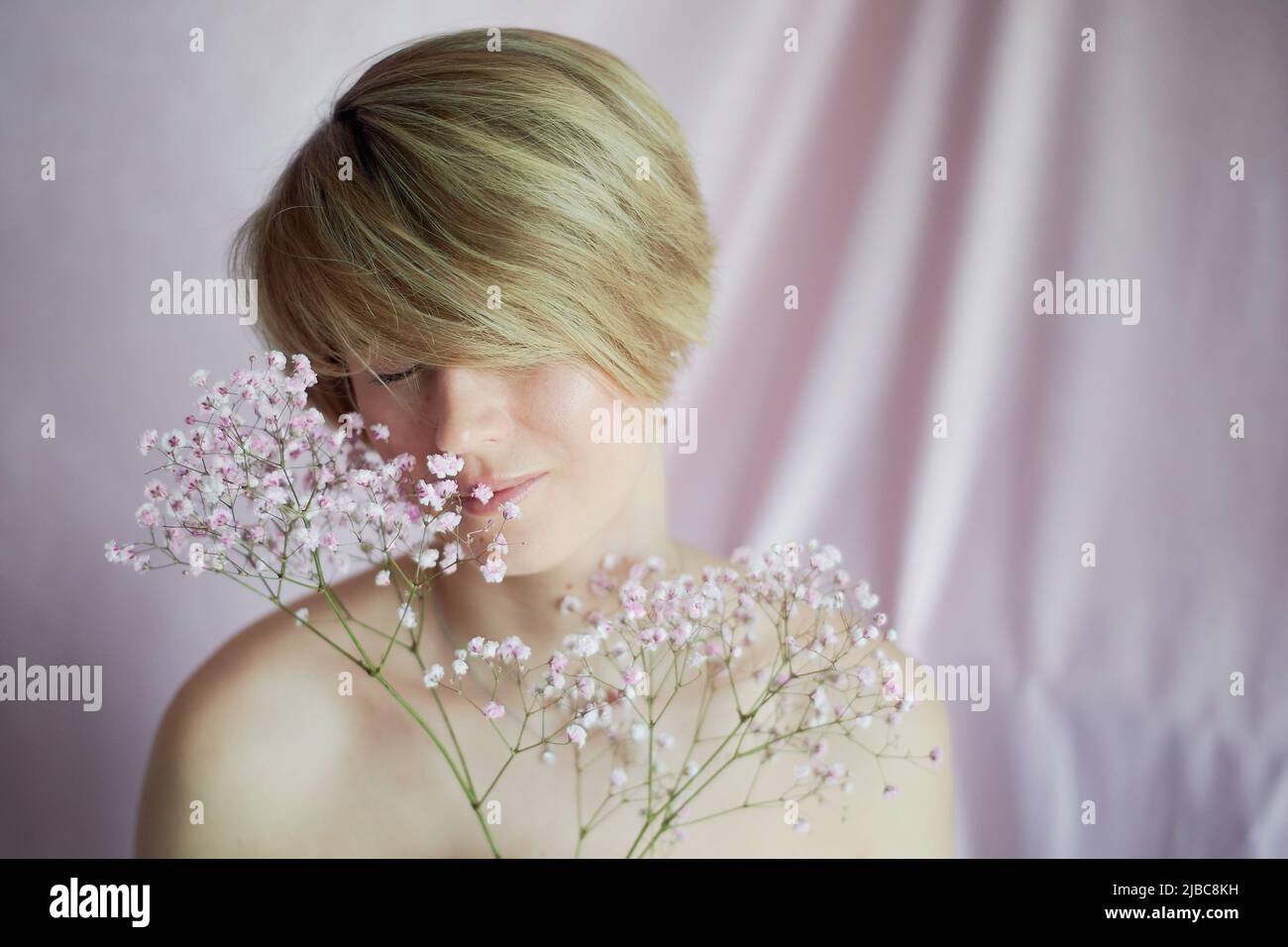 Ritratto di una ragazza su sfondo rosa con fiori. Tenerezza e femminilità. La sfera della bellezza e della salute delle donne. Taglio corto, capelli biondi Foto Stock
