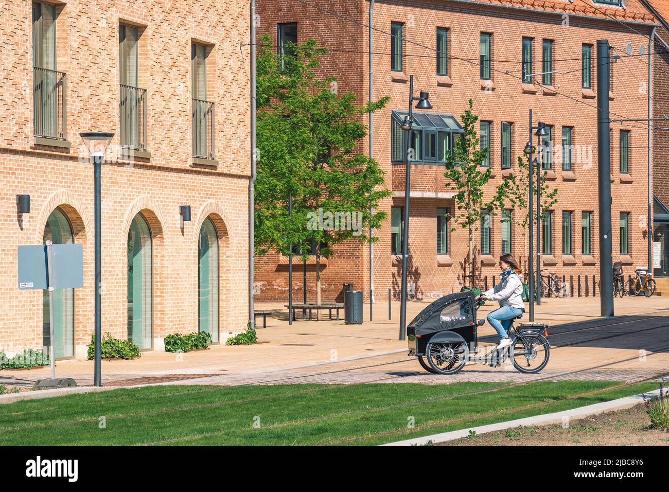 Ragazza o donna con una cargo bike su un nuovo percorso o strada tra edifici moderni nel centro di Odense, Danimarca in primavera o estate Foto Stock