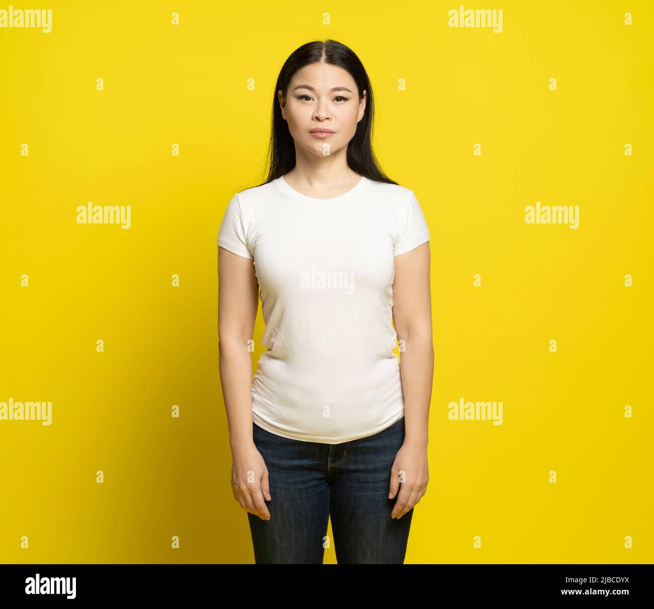 Donna asiatica triste con lunghi capelli che indossano maglietta bianca e jeans in piedi felice ridendo isolato su sfondo giallo. Concetto di moda. Foto Stock