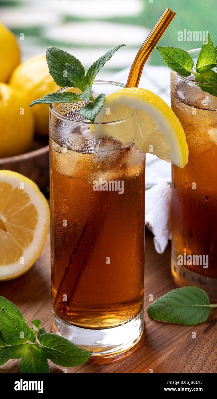 Bicchiere di tè freddo con fetta di limone, menta e cubetti di ghiaccio su tavola di legno Foto Stock