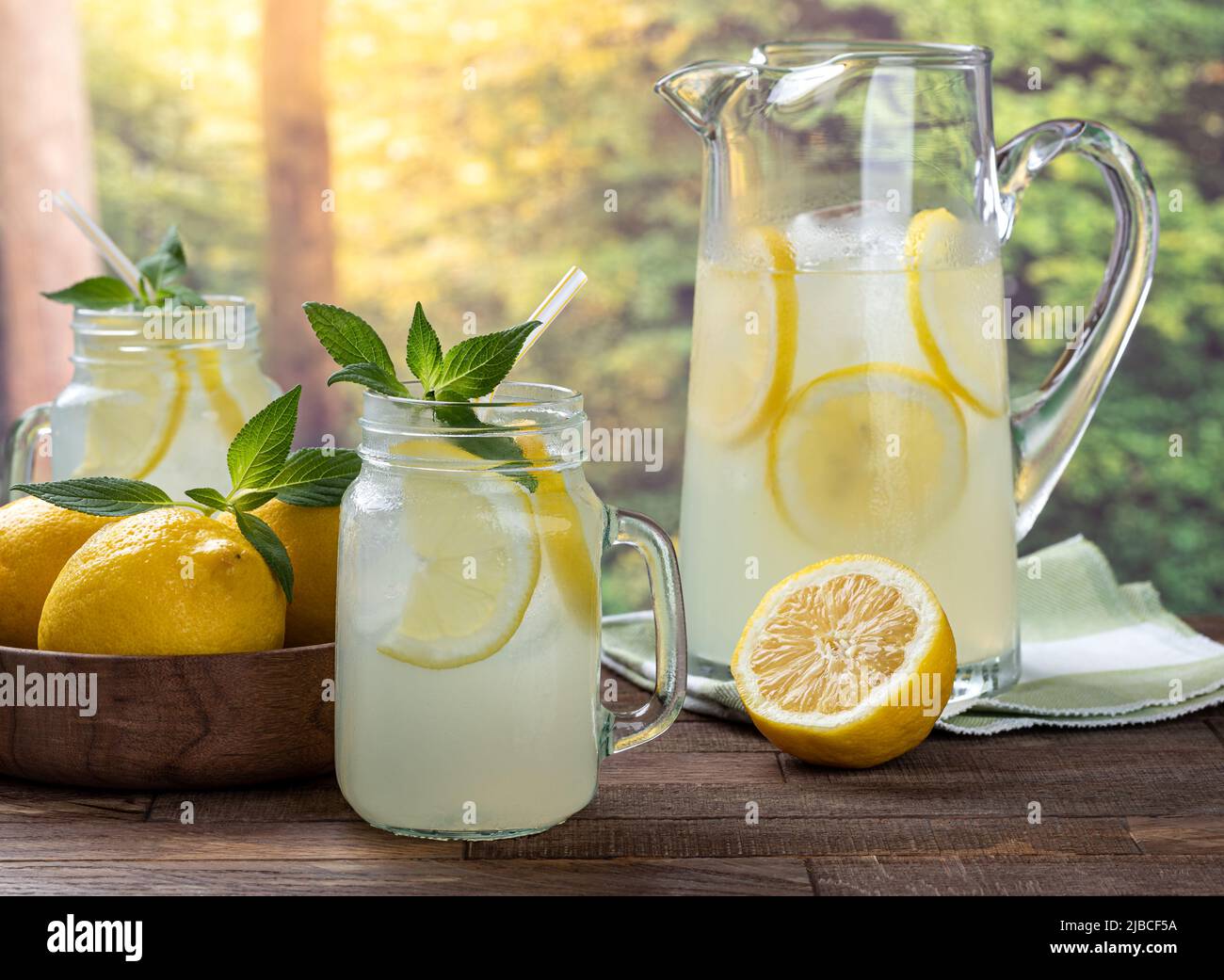 Limonata con fette di limone e menta in un bicchiere con una caraffa e limoni in bacground su un tavolo di legno con sfondo rurale Foto Stock