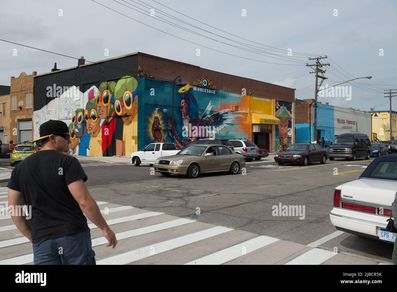Un murale colorato di persone che indossano occhiali da sole apparentemente guardando e un uomo attraversa la strada nel mercato orientale di Detroit. Foto Stock