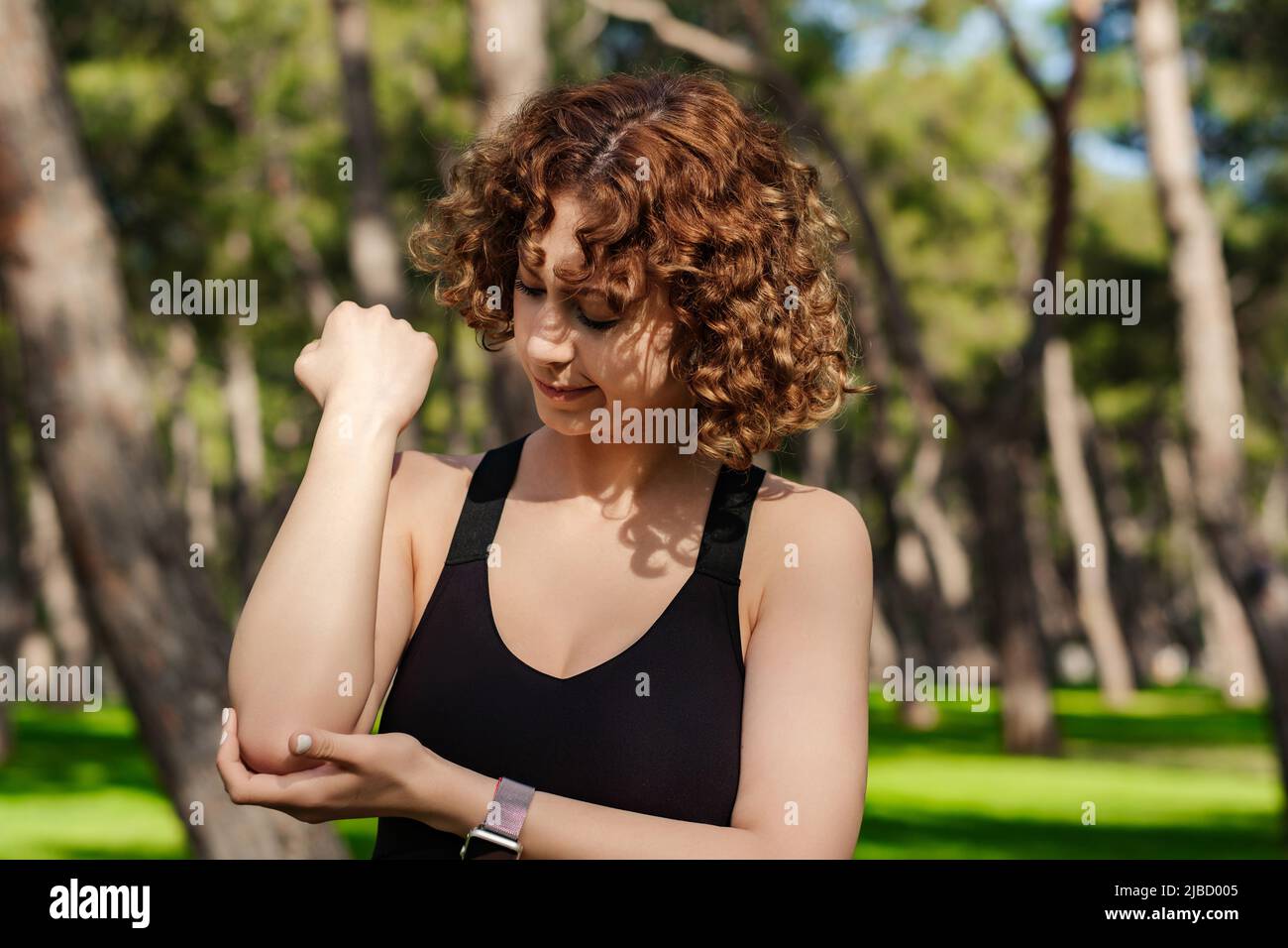 Giovane donna caucasica che indossa un reggiseno sportivo nero in piedi sul parco cittadino, all'aperto che soffre di reumatismi cronici articolari. Dolore al gomito e trattamento concep Foto Stock