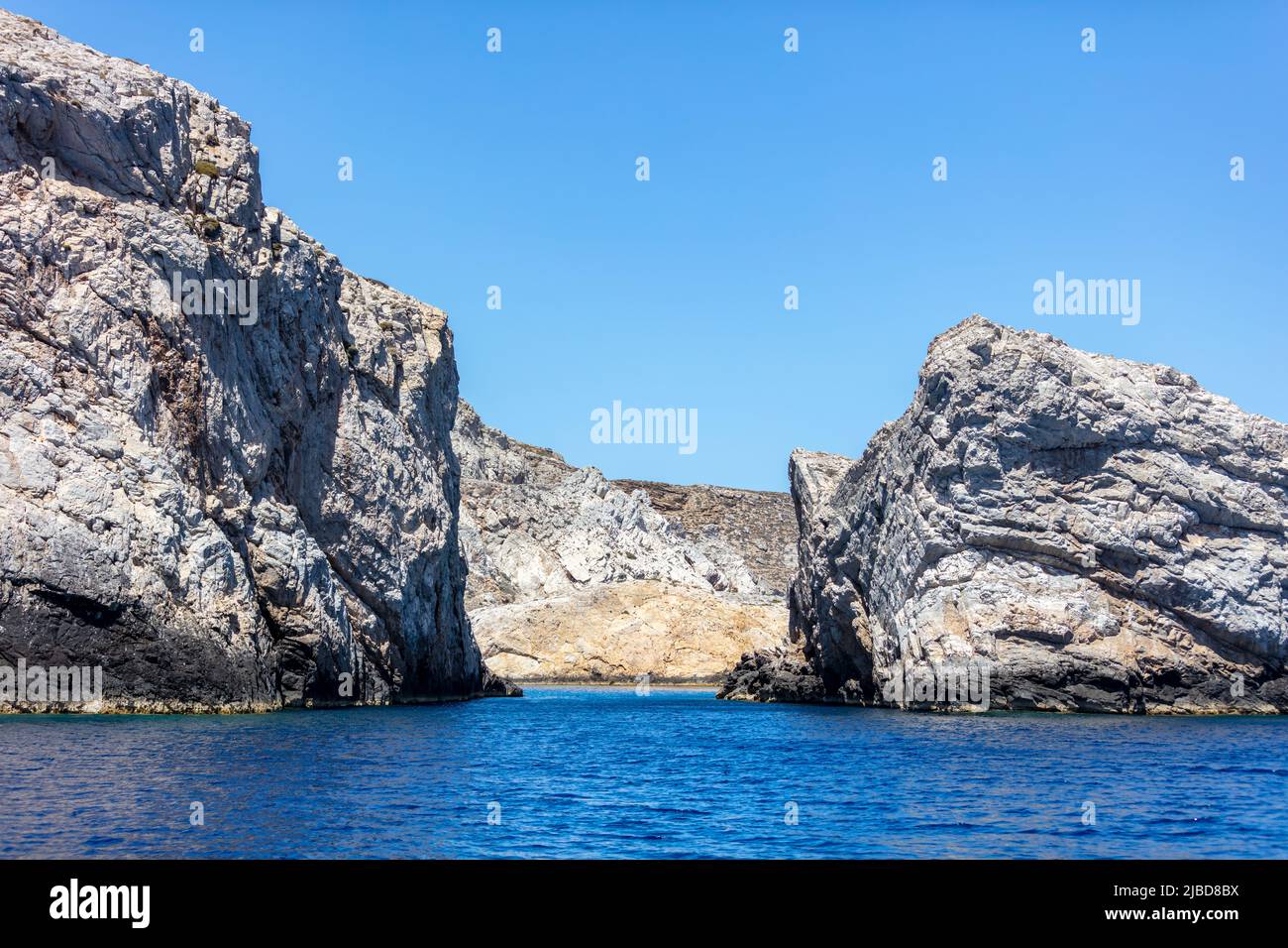 CICLADI Grecia. Formazioni rocciose, scogliere e grotte, il mar Egeo ondulato e il cielo blu chiaro sfondo. Seascape vicino all'isola di iOS, giorno di sole Foto Stock