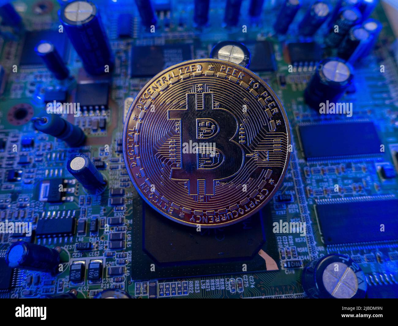 Grande bitcoin su un chip del computer di una scheda elettronica illuminata con luce blu Foto Stock