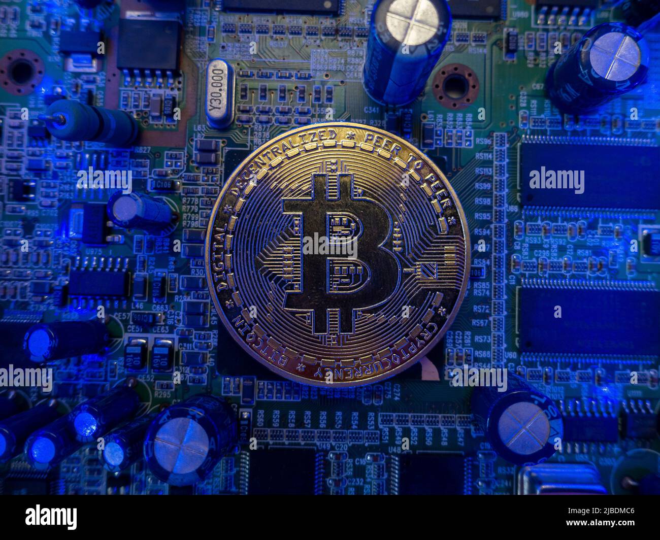 Un bitcoin d'oro con un leggero lucentezza di luce si trova tra i microchip sulla scheda madre in luce blu, un meccanismo di pagamento su Internet. Foto Stock
