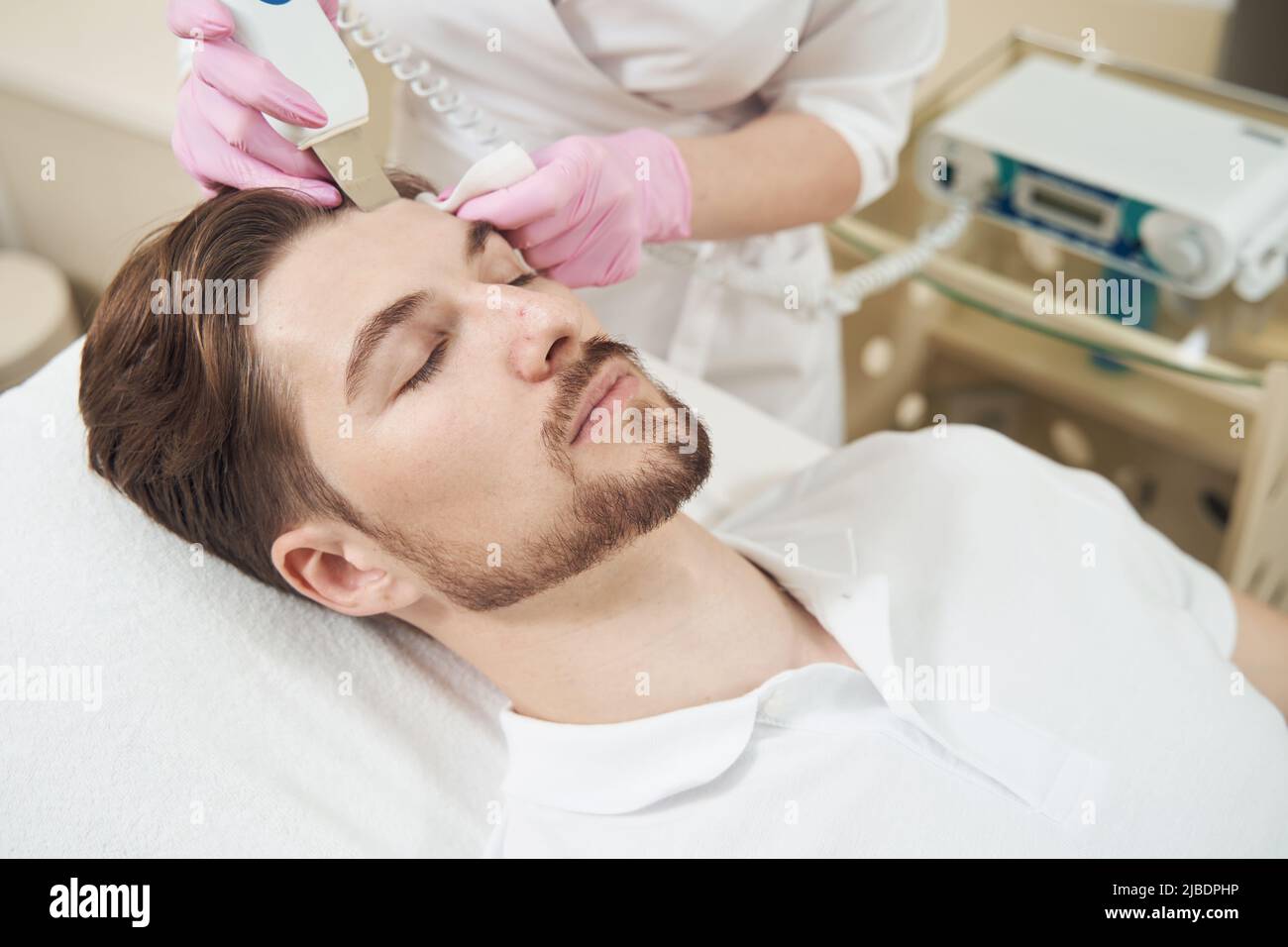 Cosmetologo che conduce la pulizia ultrasonica della fronte con l'attrezzo Foto Stock