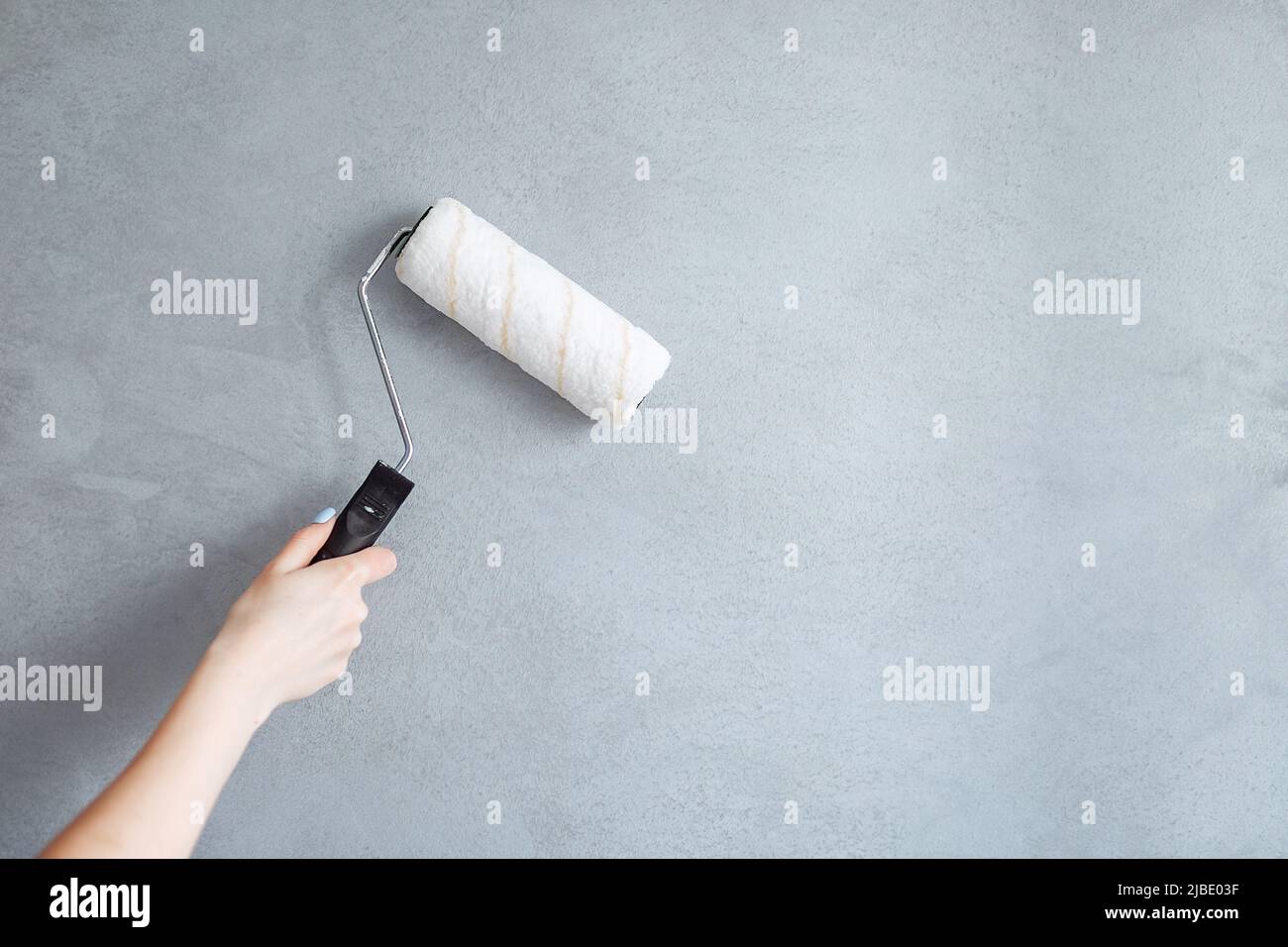 Immagine ritagliata di una mano che tiene un rullo di pittura mentre dipingi una parete della casa. Foto Stock