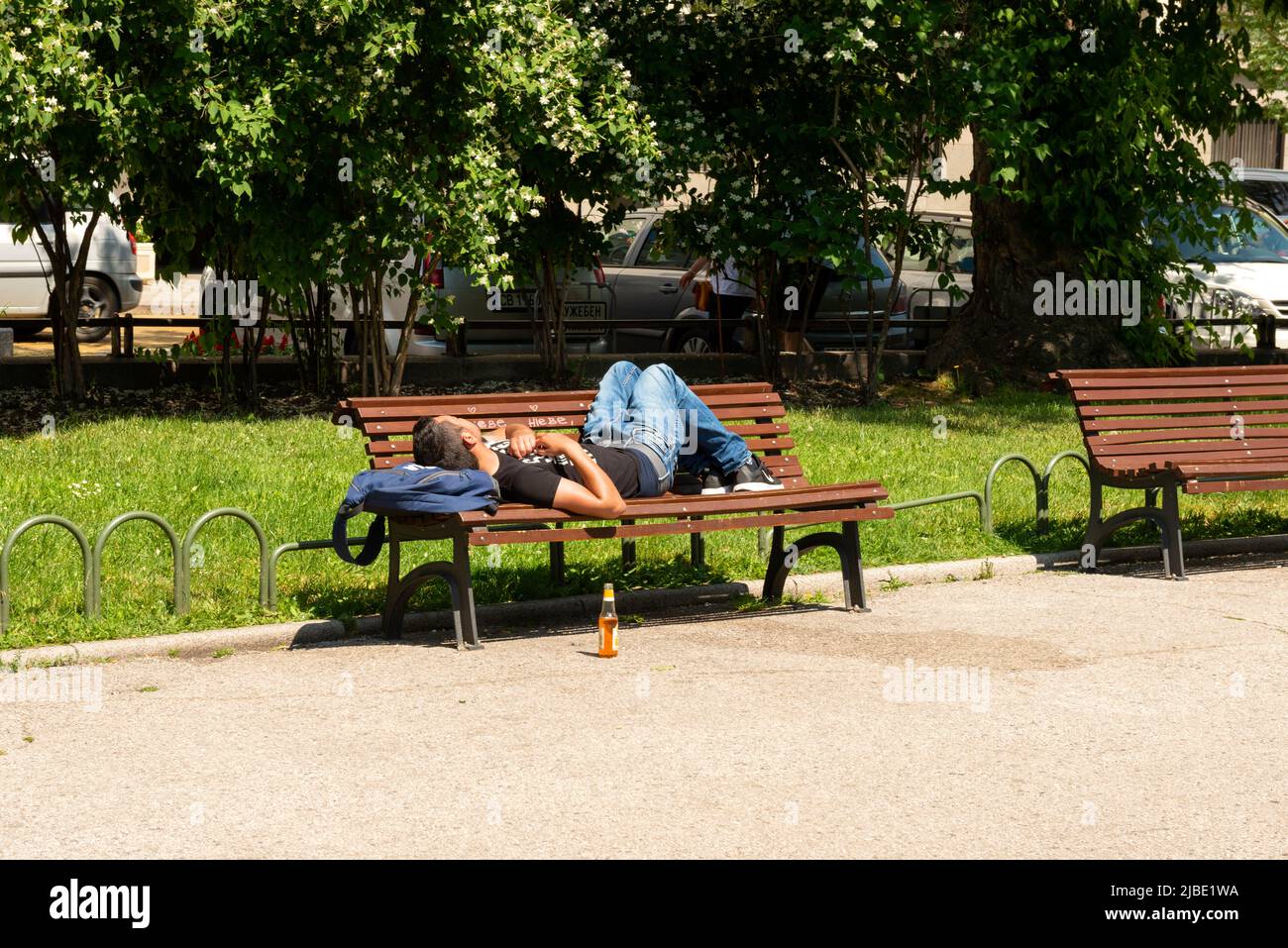 Giovane uomo che dorme su panchina nel parco pubblico in una giornata di sole a Sofia, Bulgaria, Europa dell'Est, Balcani, UE Foto Stock