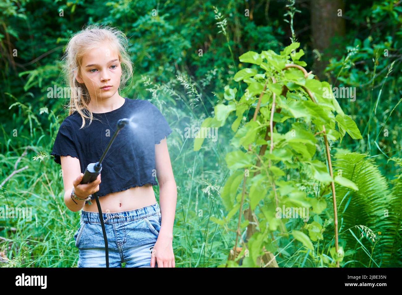 Ragazza adolescente spruzzando prodotto ecologico contro afidi e altri parassiti su alberi da frutto e altri alberi nel giardino e frutteto. Messa a fuoco selettiva Foto Stock