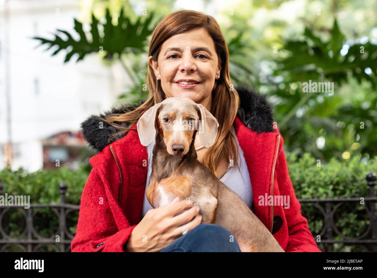 Donna latina in una giacca rossa che tiene il suo cane e guarda la macchina fotografica Foto Stock