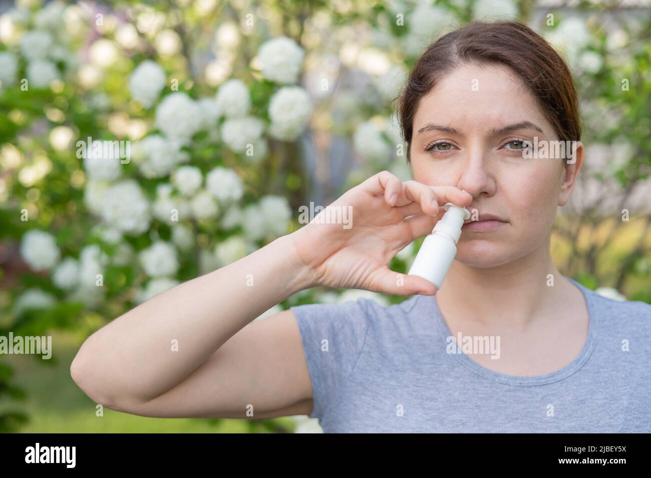 La donna caucasica usa uno spray nasale mentre cammina nel parco. Foto Stock