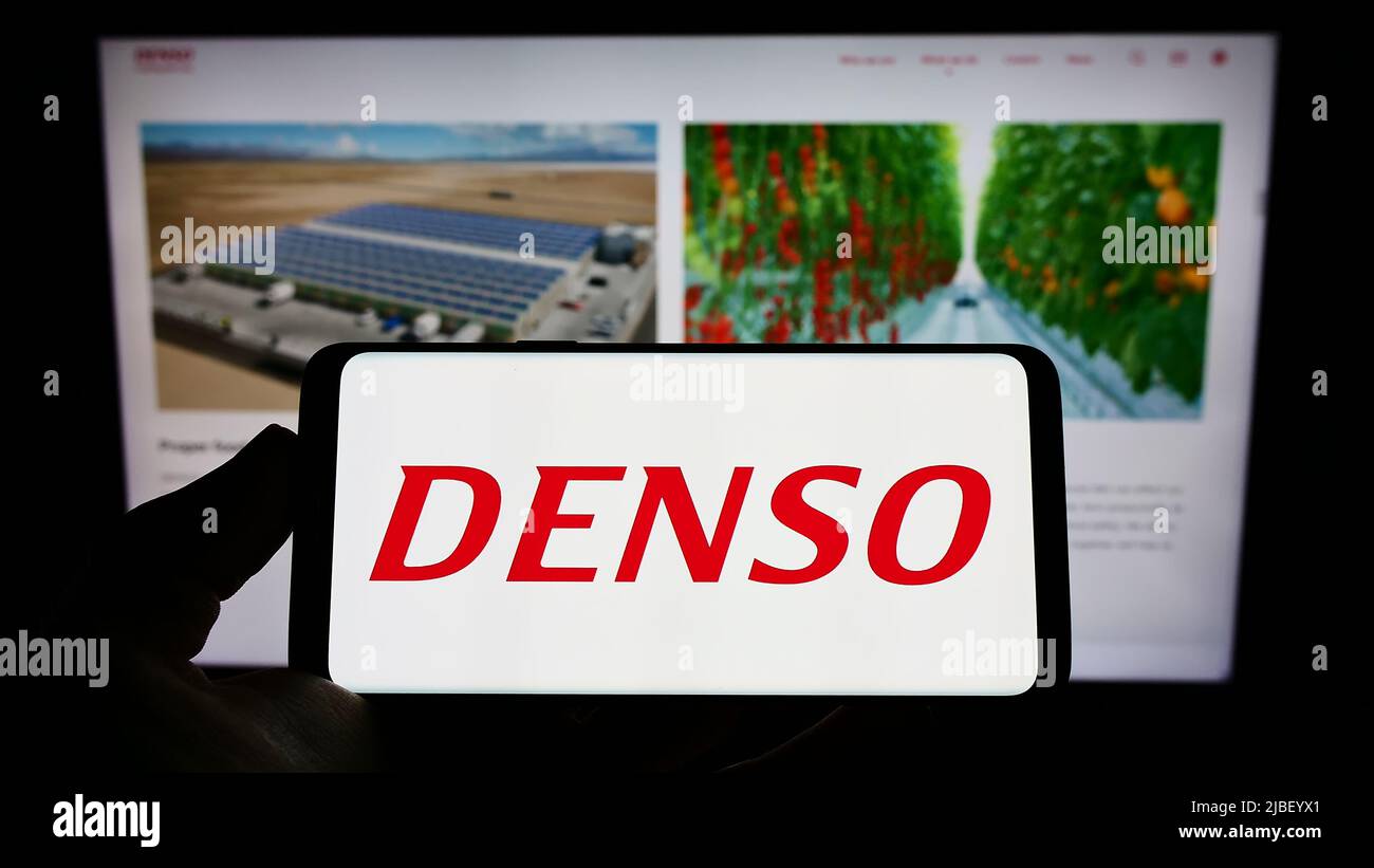 Persona che tiene il telefono cellulare con il logo della società automobilistica giapponese DENSO Corporation sullo schermo di fronte alla pagina web. Mettere a fuoco sul display del telefono. Foto Stock