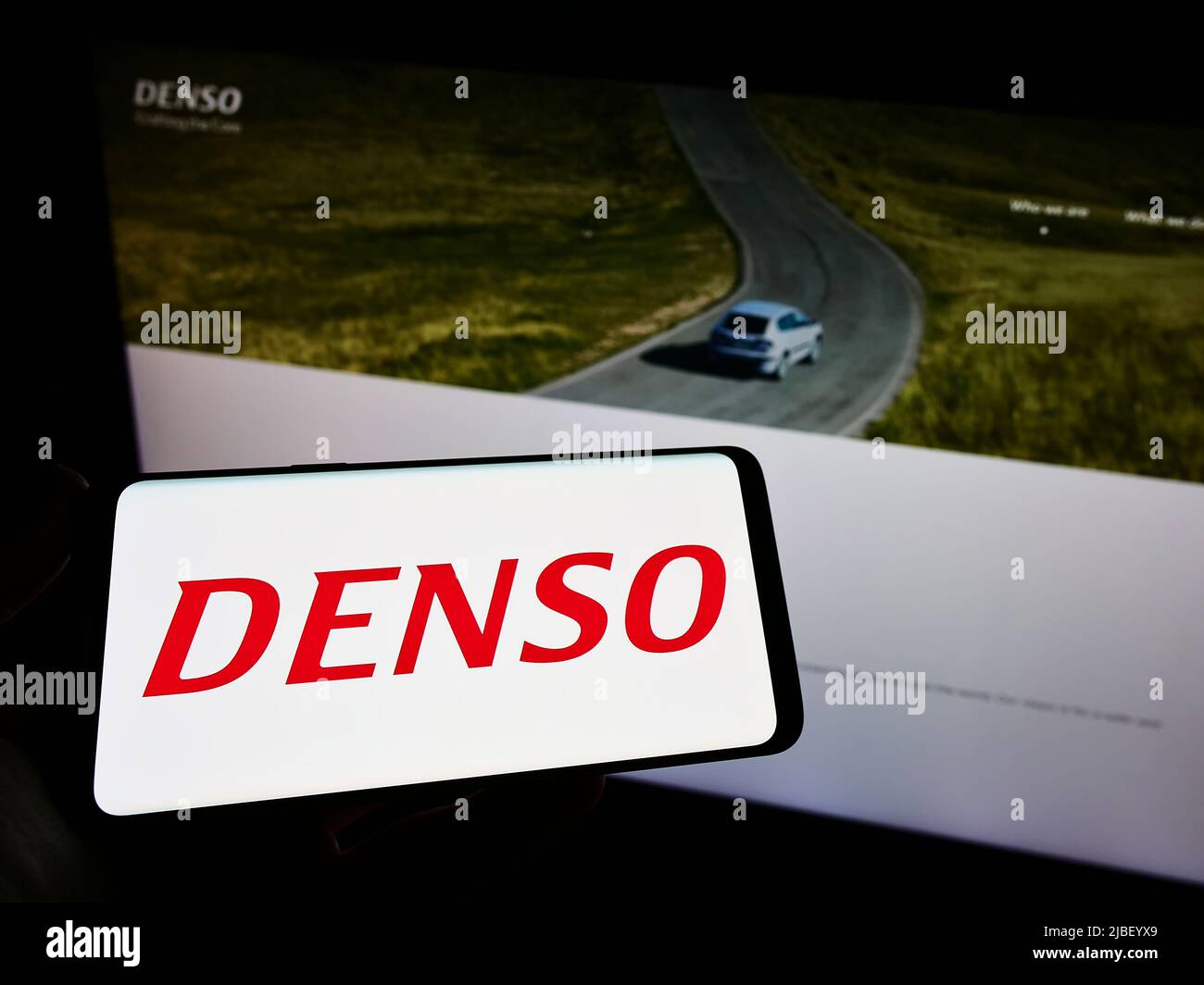 Persona che tiene il cellulare con il logo della società automobilistica giapponese DENSO Corp. Sullo schermo di fronte al sito web aziendale. Mettere a fuoco sul display del telefono. Foto Stock