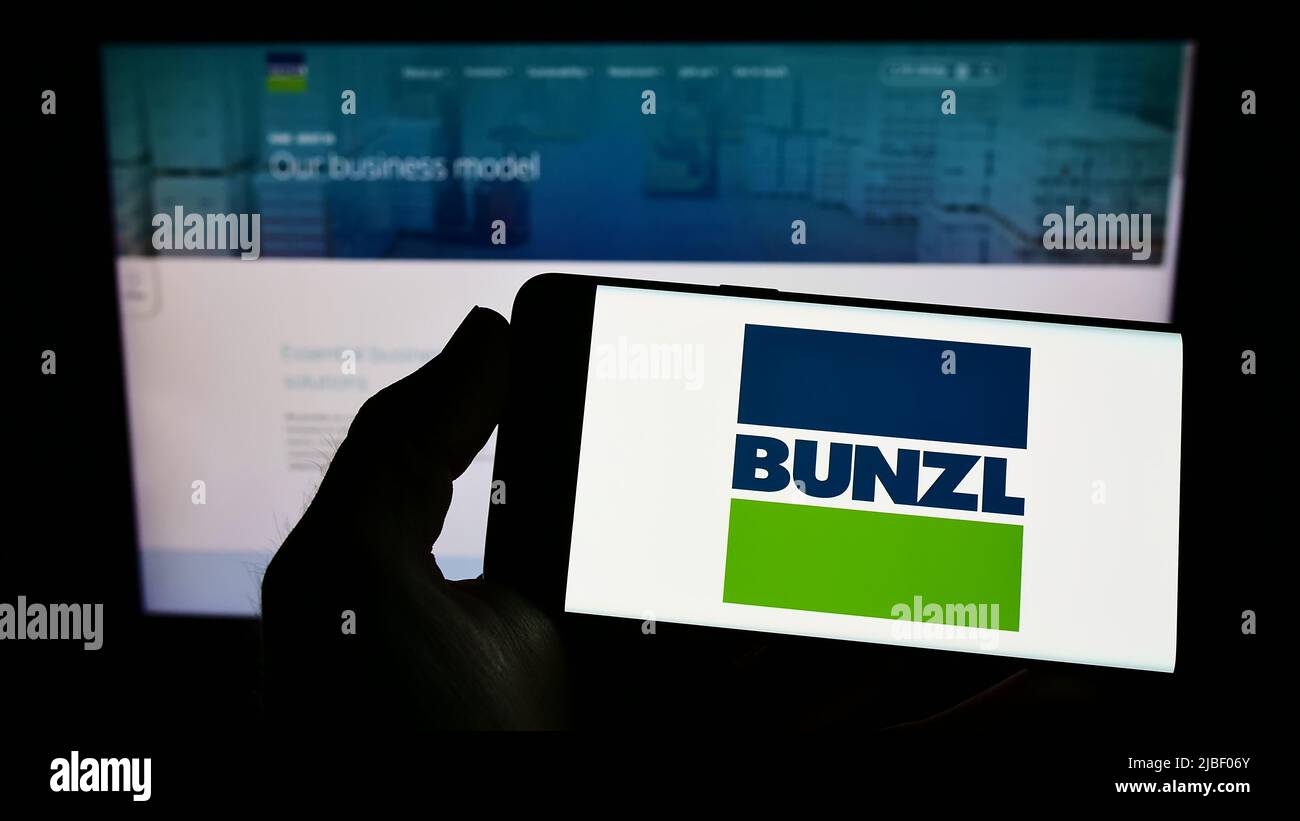 Persona che tiene uno smartphone con il logo della società di distribuzione britannica Bunzl plc sullo schermo di fronte al sito web. Mettere a fuoco sul display del telefono. Foto Stock