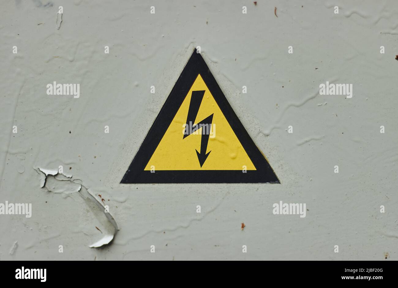 Primo piano della vecchia scatola di alimentazione incernierata grigia con segnale di pericolo giallo di elettricità in luoghi remoti Foto Stock