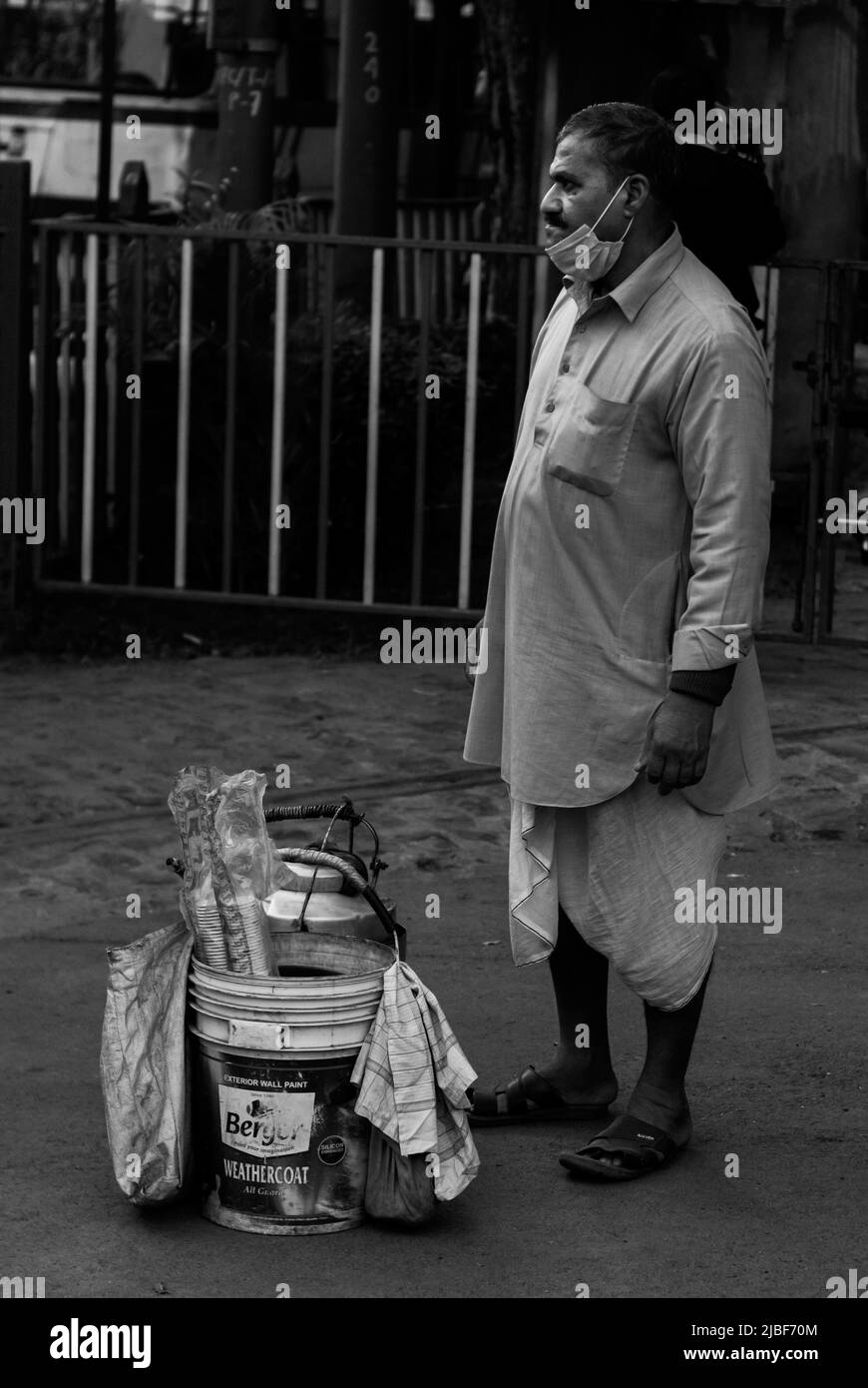 Kolkata, India - 2 gennaio 2022: Un venditore di tè che indossa dhoti indiani tradizionali, in piedi e in attesa di clienti. Un secchiello contenente bollitore per tè e caffè Foto Stock