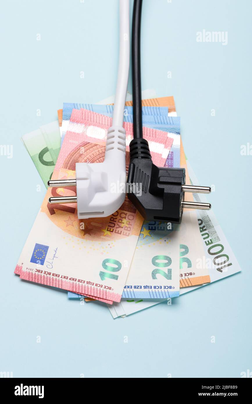 Prese elettriche sulle banconote in euro su sfondo blu. Concetto di costi dell'elettricità costosi e aumento dei prezzi delle bollette energetiche. Foto Stock