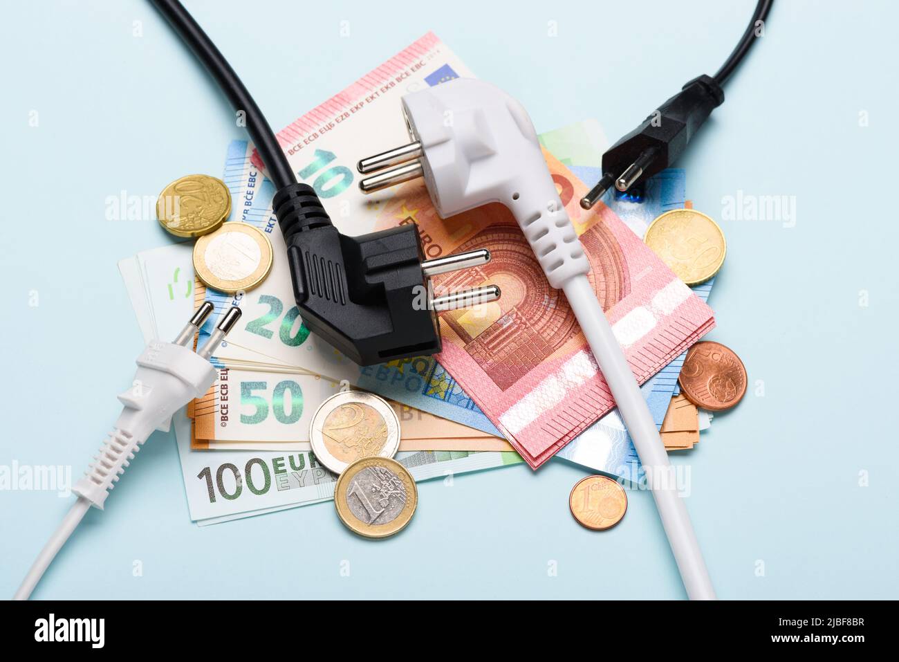 Prese elettriche sulle banconote in euro su sfondo blu. Concetto di costi dell'elettricità costosi e aumento dei prezzi delle bollette energetiche. Foto Stock