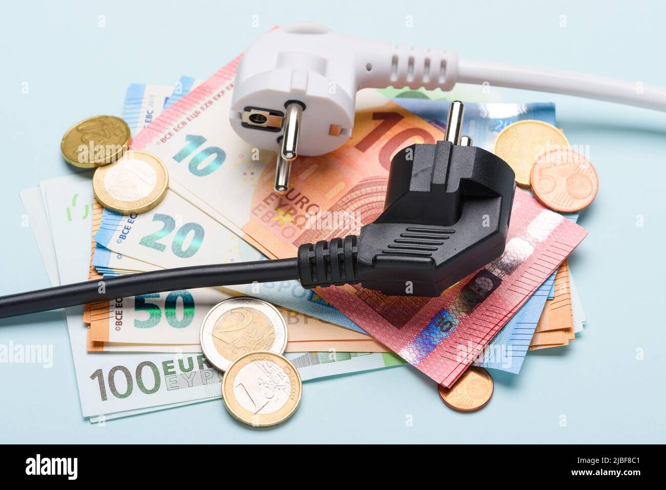 Due prese elettriche europee su banconote e monete in euro su sfondo blu. Concetto di costi dell'elettricità costosi e aumento del prezzo della bolletta energetica Foto Stock
