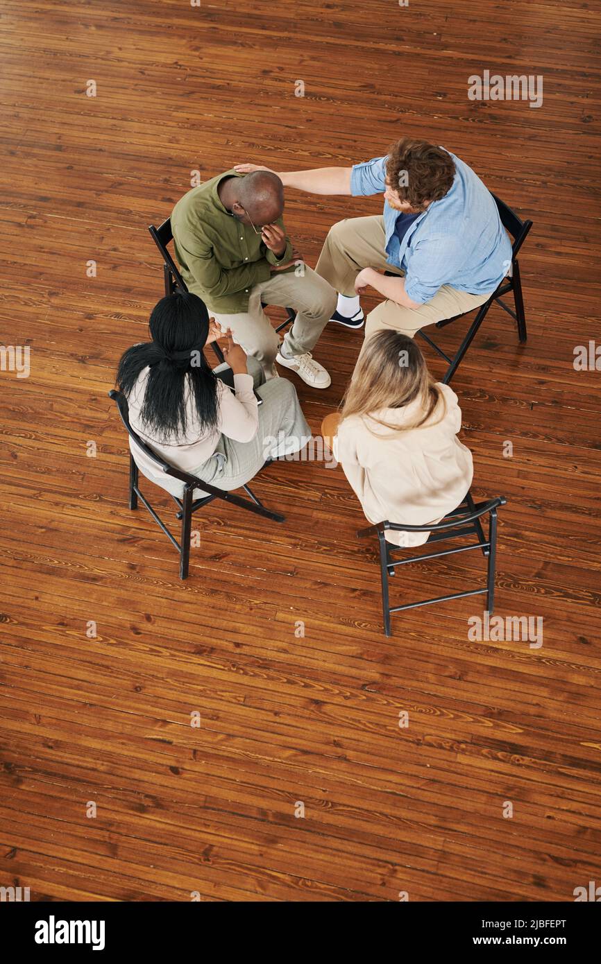 Sopra la vista delle persone interrazziali che sostengono l'uomo afro-americano durante la sessione mentre frequentano il corso di riabilitazione psicologica Foto Stock