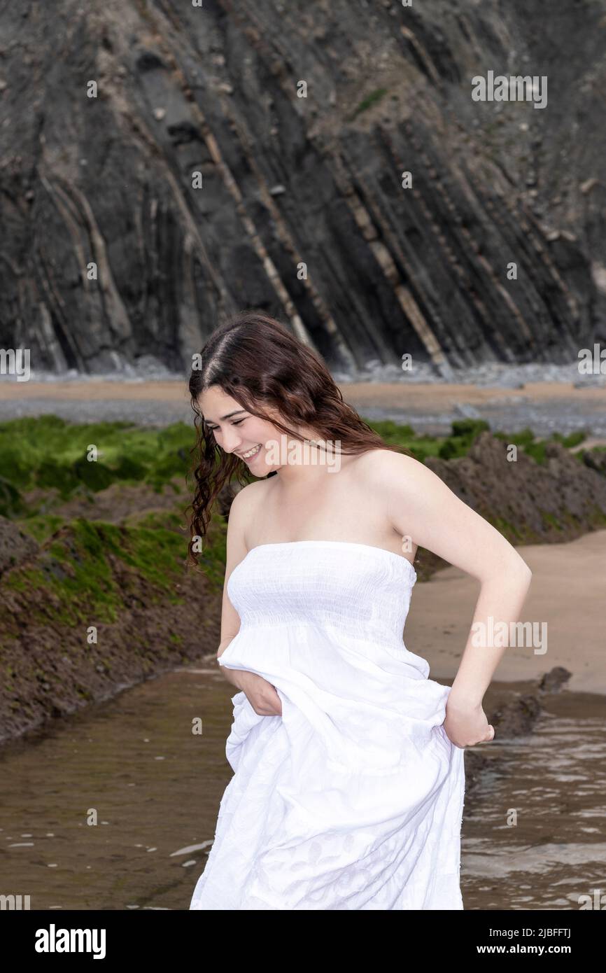donna brunetta in abito bianco che ride sulla spiaggia Foto Stock