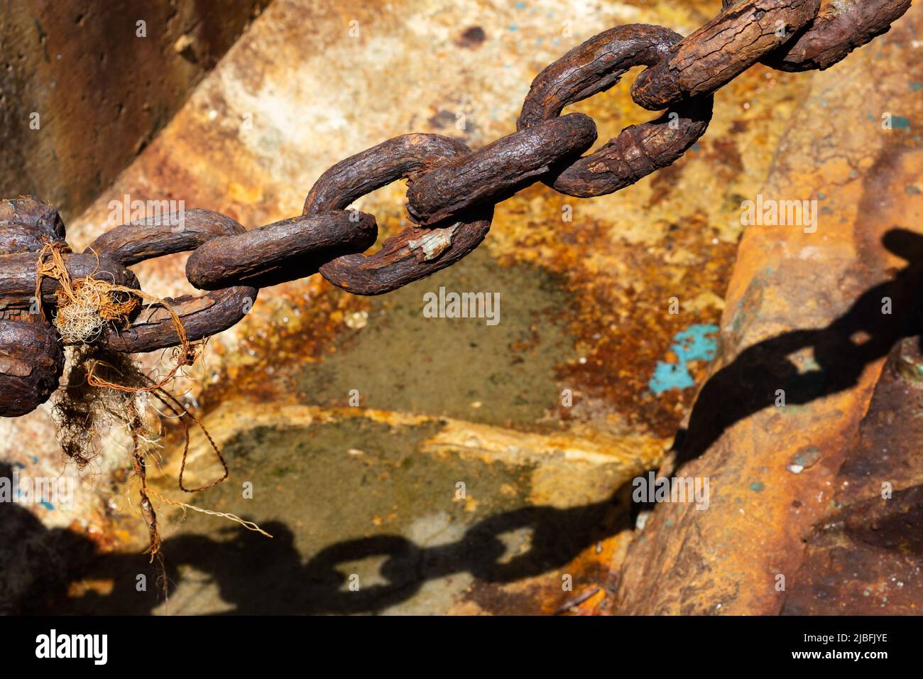 Catena di metallo arrugginita appesa vicino ad un molo. La catena proietta un'ombra. Foto Stock