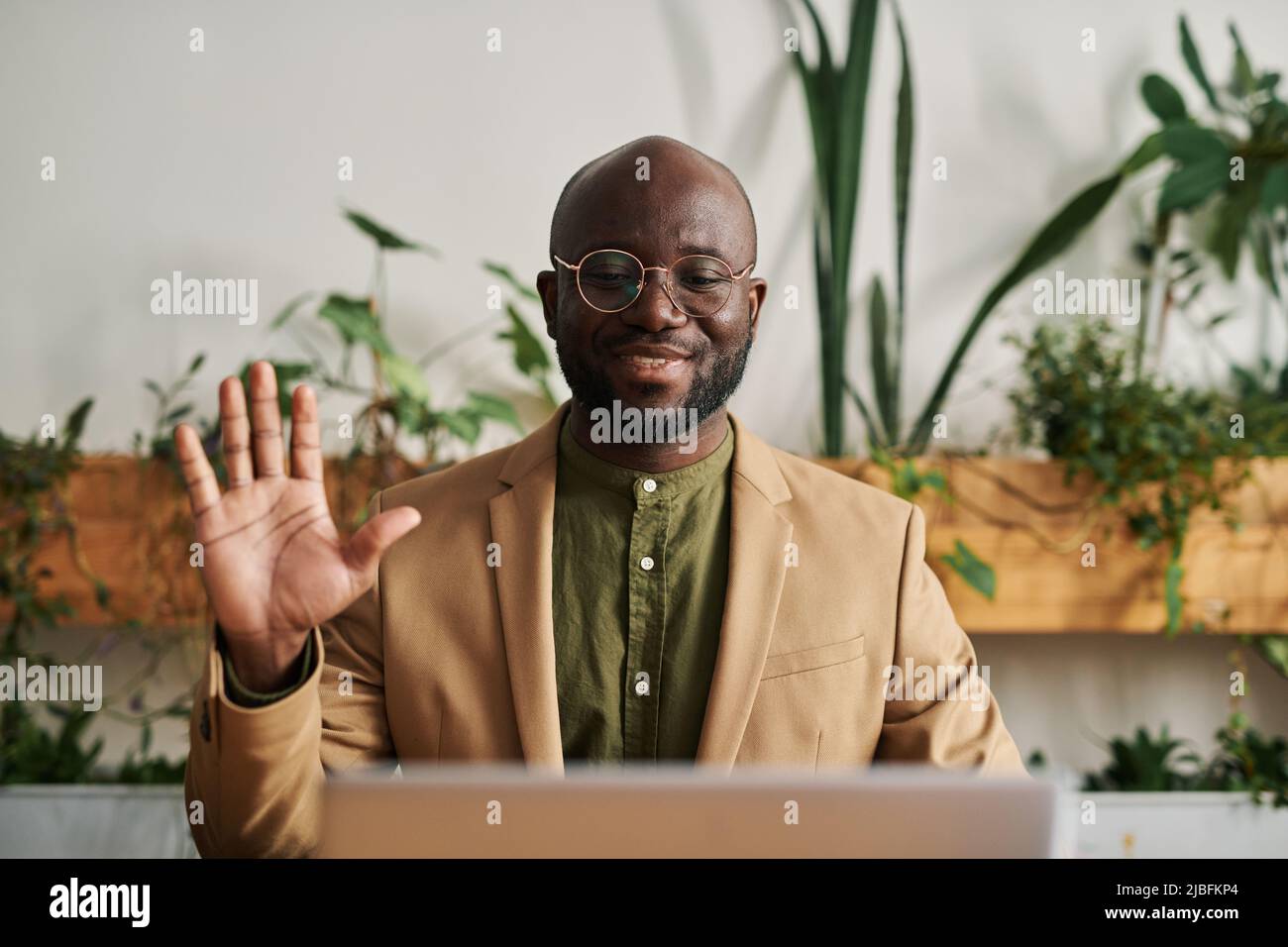 Il giovane psicoterapeuta o consigliere di successo saluta il paziente sullo schermo del laptop durante la sessione psicologica online nel suo ufficio Foto Stock